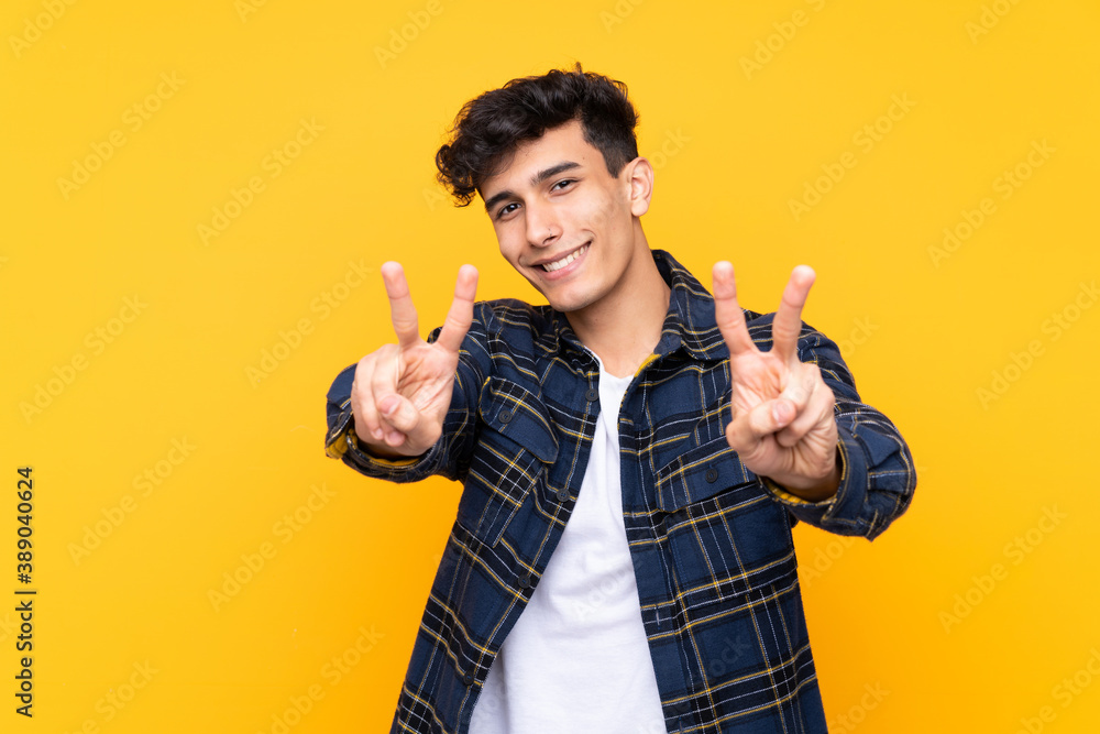 Young Argentinian man over isolated yellow background smiling and showing victory sign Young Argentinian man over isolated yellow background smiling and showing victory sign
