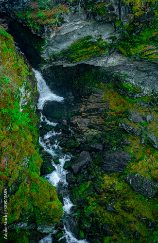 Waterfall running through a deep gorge surrounded by lush green vegetation. Seen from above.