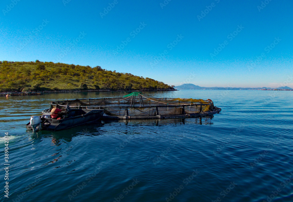 man working on fish farm with ponds nets boats at sea with mountain background