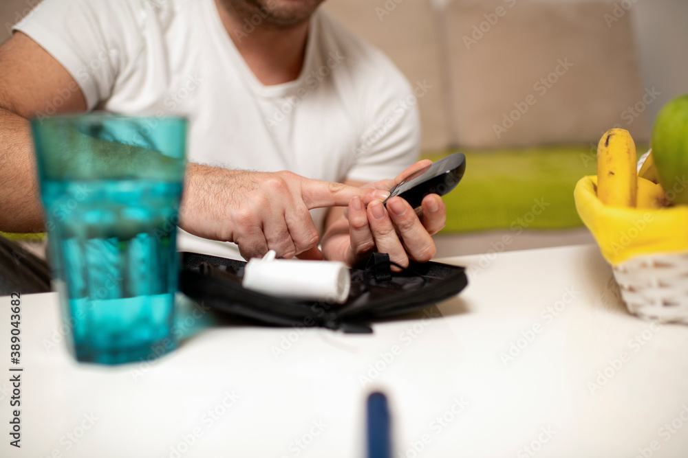 Young man checking his blood sugar levels while sitting on the sofa at home Young man checking his blood sugar levels while sitting on the sofa at home