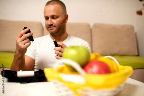 Young man checking his blood sugar levels while sitting on the sofa at home