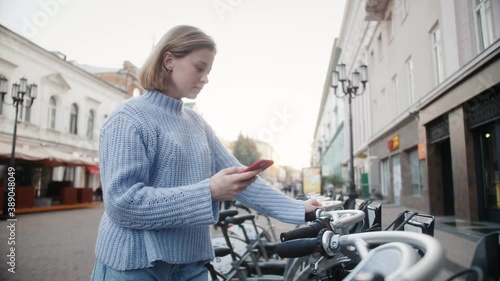 Bicycles for rent in the city center. Woman takes bike bicycle in sharing parking lot, phone application for rent bike.