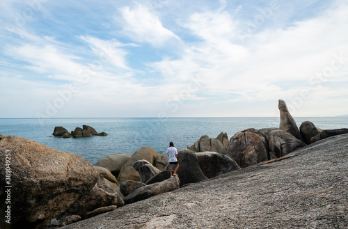 Young Man with a long hair in a white t-shirt, standing on a rock and enjoying a view on a sea. Traveling.