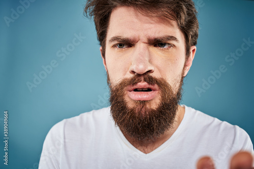 Bearded man displeased facial expression emotions close-up blue background white t-shirt