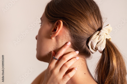 Blond woman with her hand touching her neck, rose ring on her finger. Side view.