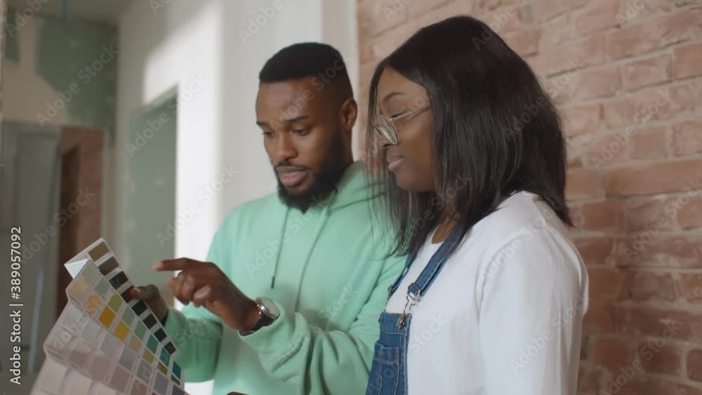 Young african couple looking at color samples at home choosing paint for wall Young african couple looking at color samples at home choosing paint for wall