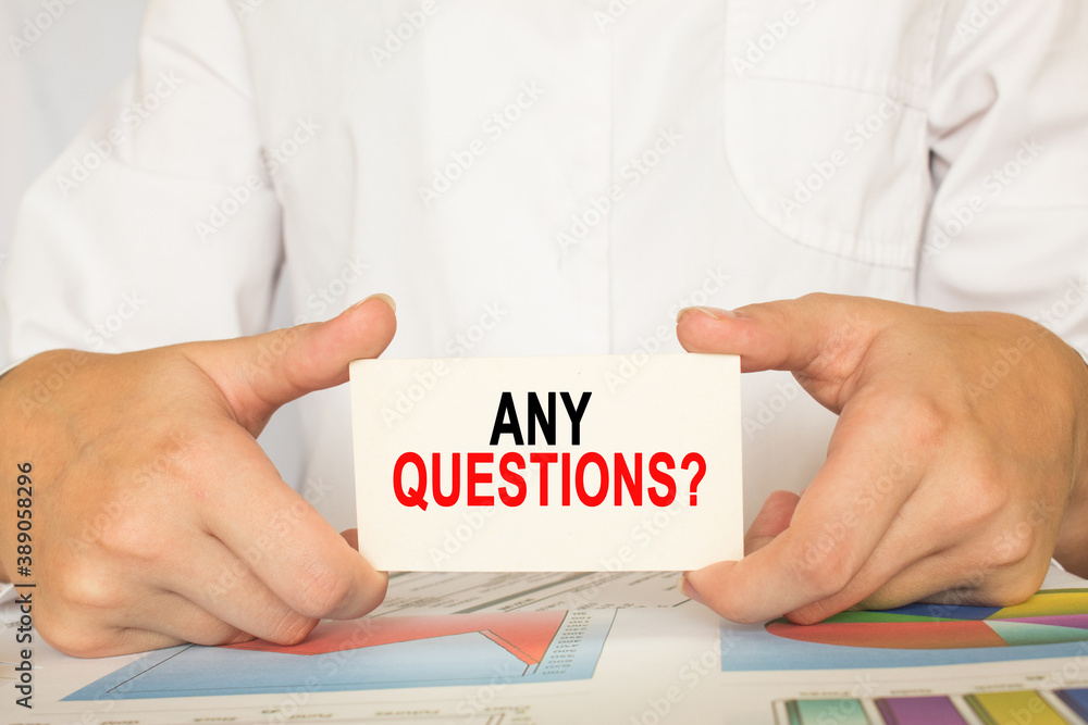 a man in the office holds a card with text ANY QUESTIONS . business concept a man in the office holds a card with text ANY QUESTIONS . business concept