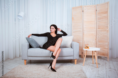 Girl in a black dress sits on a gray sofa