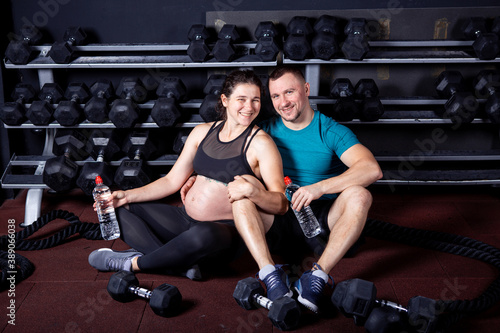 Pregnant woman goes for sports with her husband in gym for cross training. Couple athletes expecting baby while resting after training and exercises to strengthen health and muscles expectant mother