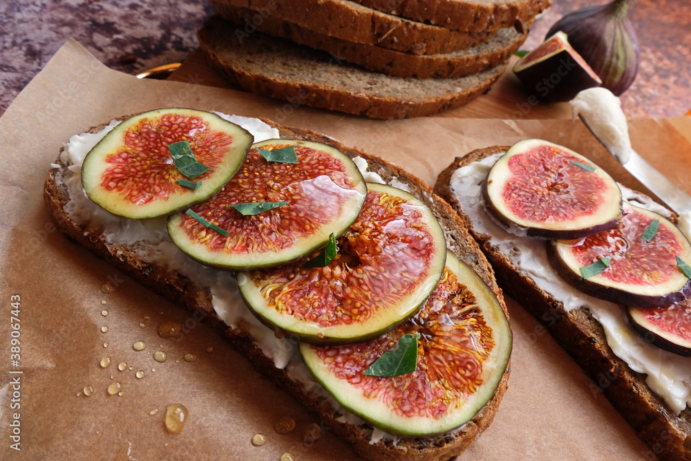 Figs. Sandwiches with figs, cheese, arugula, honey and nuts on wooden board over textured purple backdrop. Homemade. Everyday autumn kitchen. Vertical. Figs. Sandwiches with figs, cheese, arugula, honey and nuts on wooden board over textured purple backdrop. Homemade. Everyday autumn kitchen. Vertical.