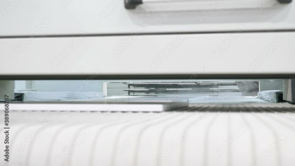 Worker in gloves takes painted white boards from modern automatic machine at bright light in production workshop closeup Worker in gloves takes painted white boards from modern automatic machine at bright light in production workshop closeup