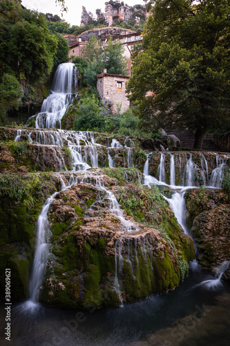 Beautiful tall waterfall that falls from the height of the city of Orbaneja del Castillo and the water flows over the rocks covered with vegetation, Burgos, Spain