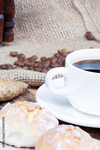 A white cup of coffee and cake on a wooden background. Coffee beens on a linen fabric. Cone. Vertical view