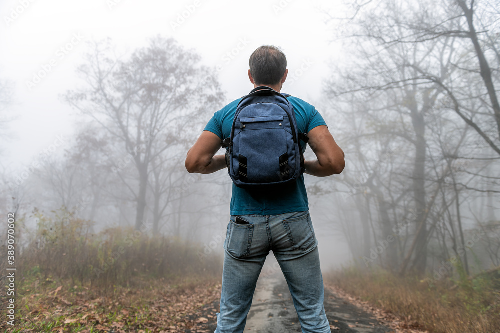 Naklejka premium Back of young man hiker hiking on Cedar Cliffs forest woods trail in Wintergreen Resort, Virginia standing looking at view in morning fog, foggy weather