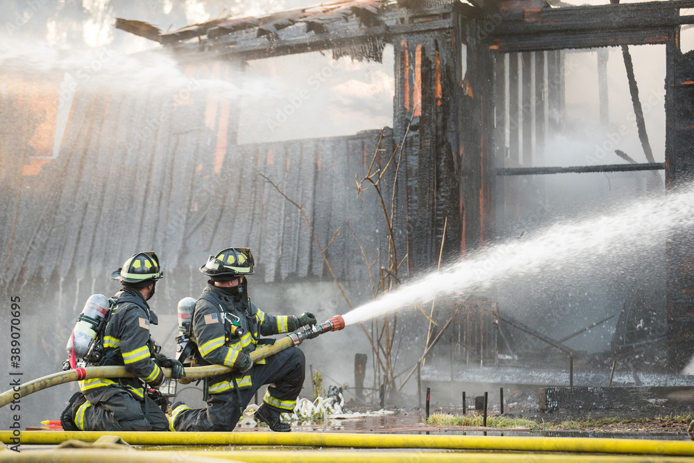 A residential home burns in a house fire as firefighters spay water from a hose in an effort to put it out.