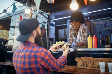 polite female employee holding, giving, two sandwiches to a satisfied beardy customer. fast food service