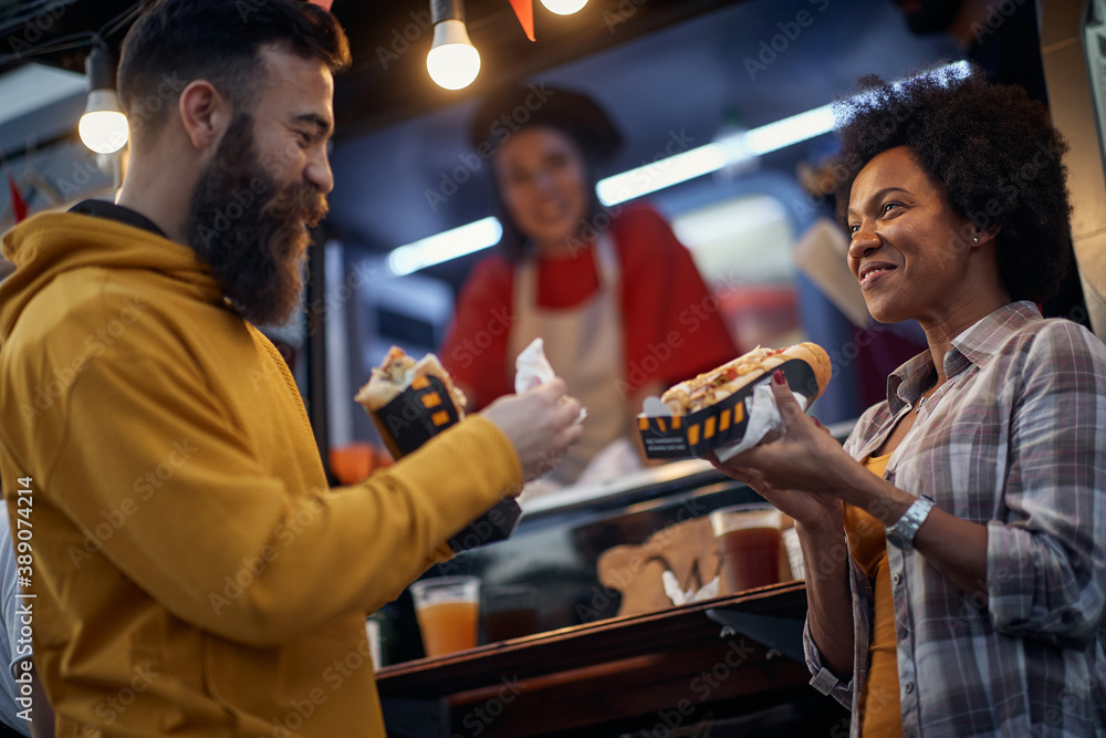 friends talking and smiling while eating sandwiches in front of fast food service