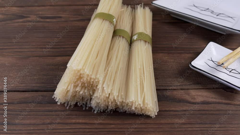 Dry unprocessed rice noodles and white square plate next to chopsticks on wooden background