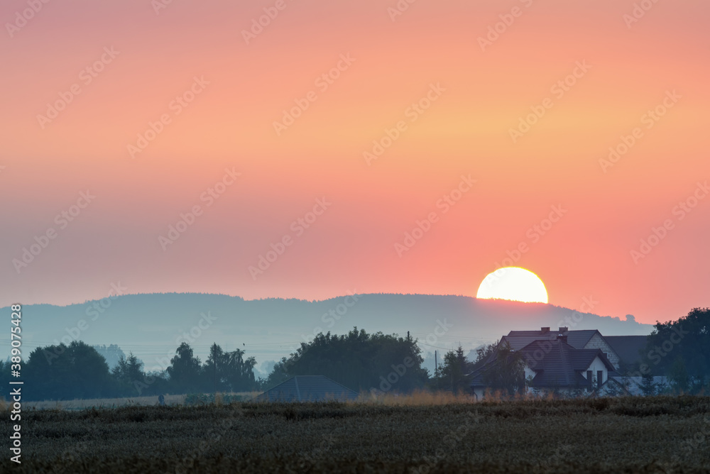 shield of the rising sun over hills and village