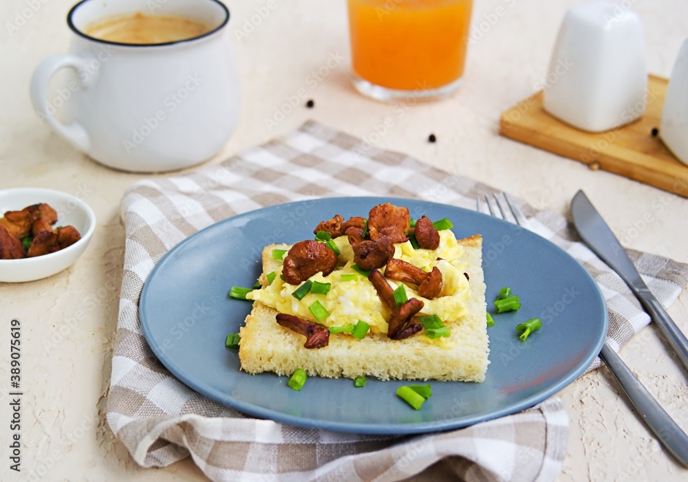 Tender scramble omelet on crispy white bread toast with fried chanterelles on a gray plate