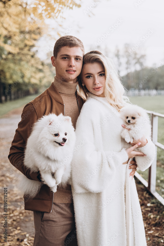 Beautiful young couple in autumn walks with dogs, pomeranian, in the park Beautiful young couple in autumn walks with dogs, pomeranian, in the park