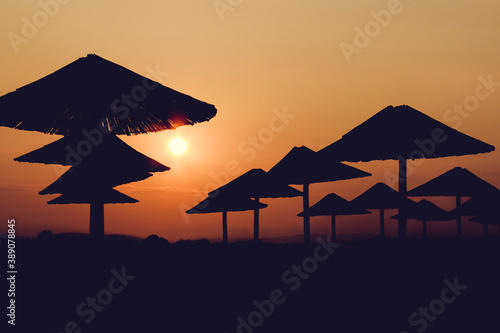 The sunset red sun illuminates the beach silhouette straw umbrellas