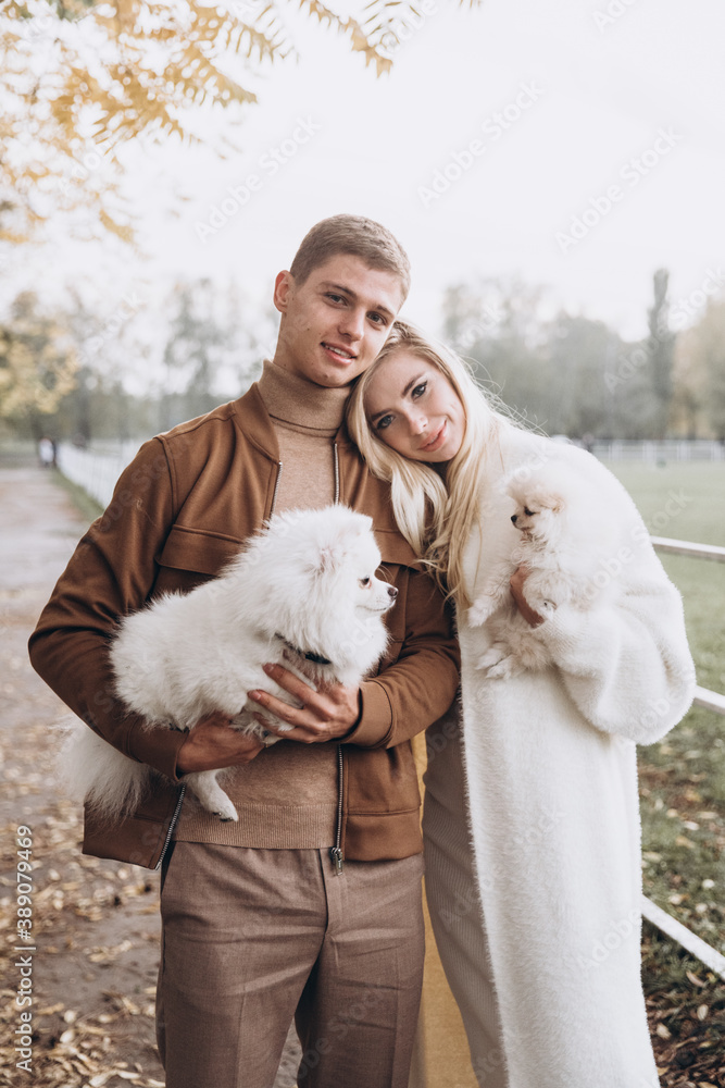 Beautiful young couple in autumn walks with dogs, pomeranian, in the park Beautiful young couple in autumn walks with dogs, pomeranian, in the park