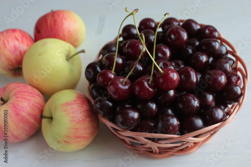 Ripe cherries in a bowl and apples on a wooden table.