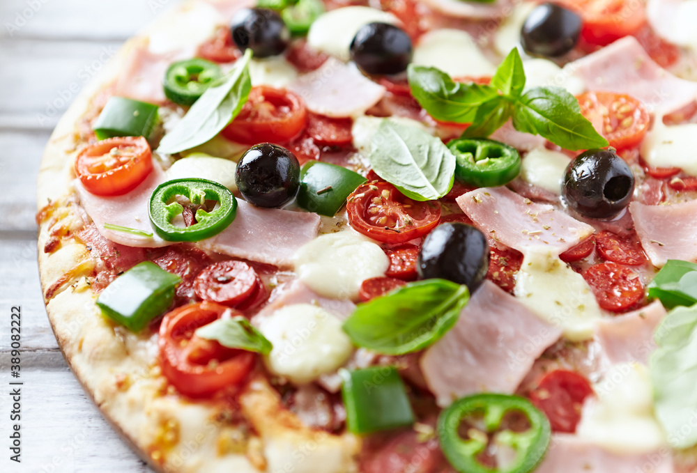 Pizza with ham, mozzarella cheese, cherry tomatoes, green and jalapeno pepper, black olives and fresh basil. Bright background. Close up. Pizza with ham, mozzarella cheese, cherry tomatoes, green and jalapeno pepper, black olives and fresh basil. Bright background. Close up.