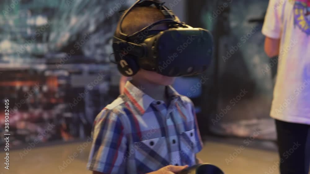 The boy plays a computer game in virtual reality glasses in a gaming club. The boy plays a computer game in virtual reality glasses in a gaming club.