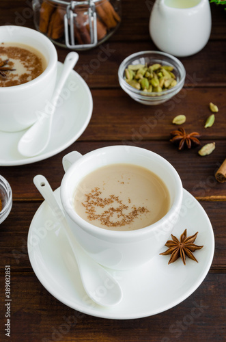 Hot tea with milk, cinnamon, cardamom, anise and other spices, Indian masala tea in a white cup on a wooden background. copy space.