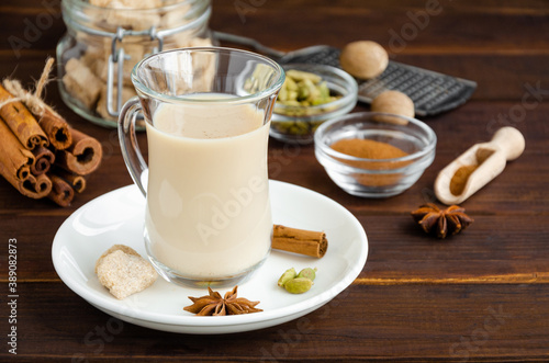 Hot tea with milk, cinnamon, cardamom, anise and other spices, Indian masala tea in a glass cup on a wooden background. copy space.