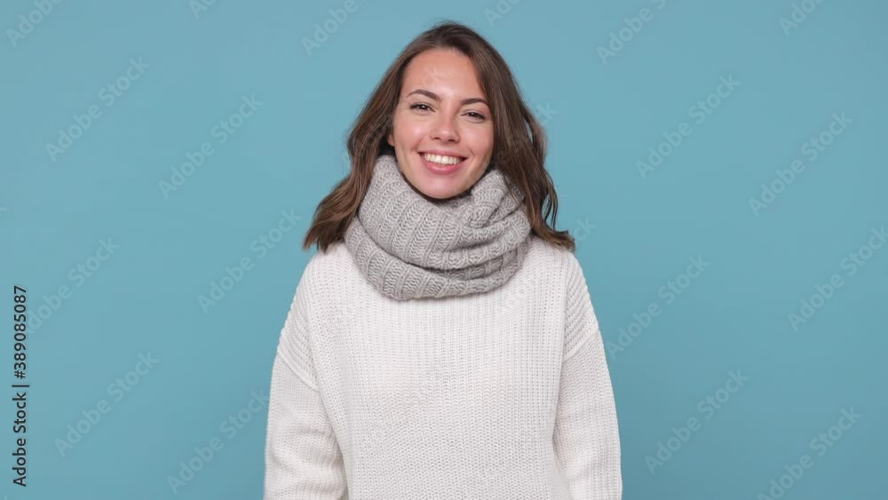 Smiling young woman in sweater scarf isolated on blue background studio. Healthy lifestyle ill sick treatment cold season concept. Point finger on camera doing phone gesture says call me back blinking Smiling young woman in sweater scarf isolated on blue background studio. Healthy lifestyle ill sick treatment cold season concept. Point finger on camera doing phone gesture says call me back blinking