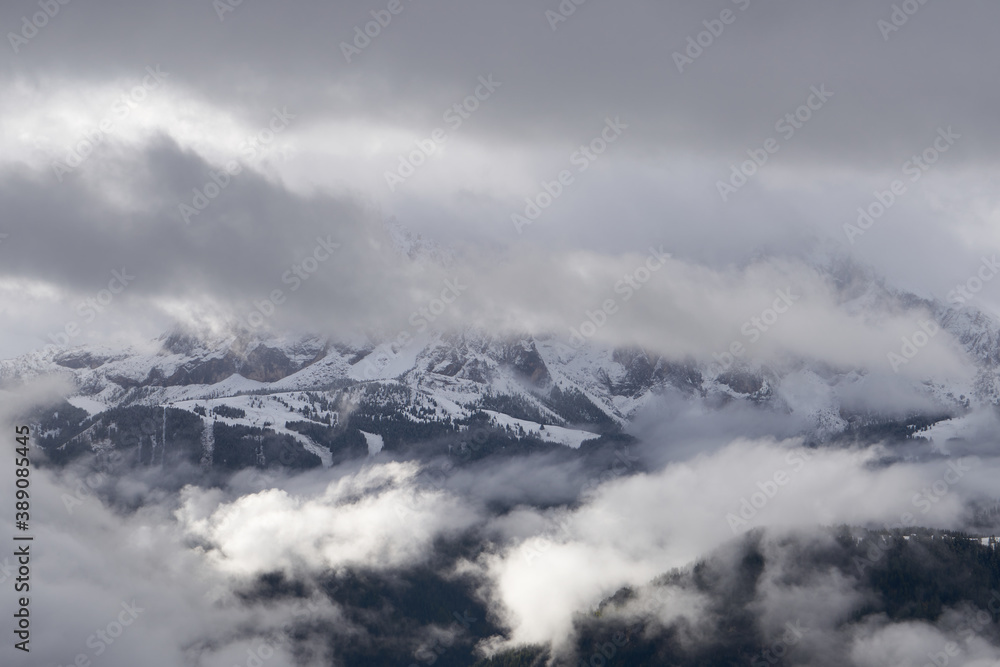 Forested mountain slope in low lying cloud with the evergreen conifers shrouded in mist in a scenic landscape view and snow in the dolomites
