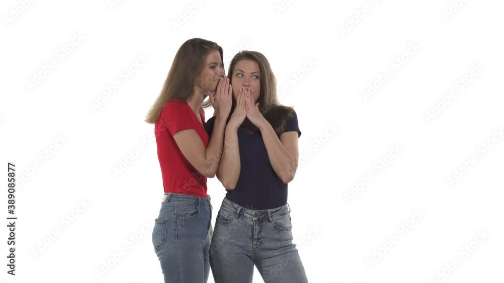 Portrait of Caucasian twin sisters. Woman in red t-shirt whispering gossip or sharing secret to her astonished sister. Isolated on white background Portrait of Caucasian twin sisters. Woman in red t-shirt whispering gossip or sharing secret to her astonished sister. Isolated on white background