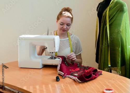 woman working with white sewing machine on wooden table near mannequin in taloring studio photo