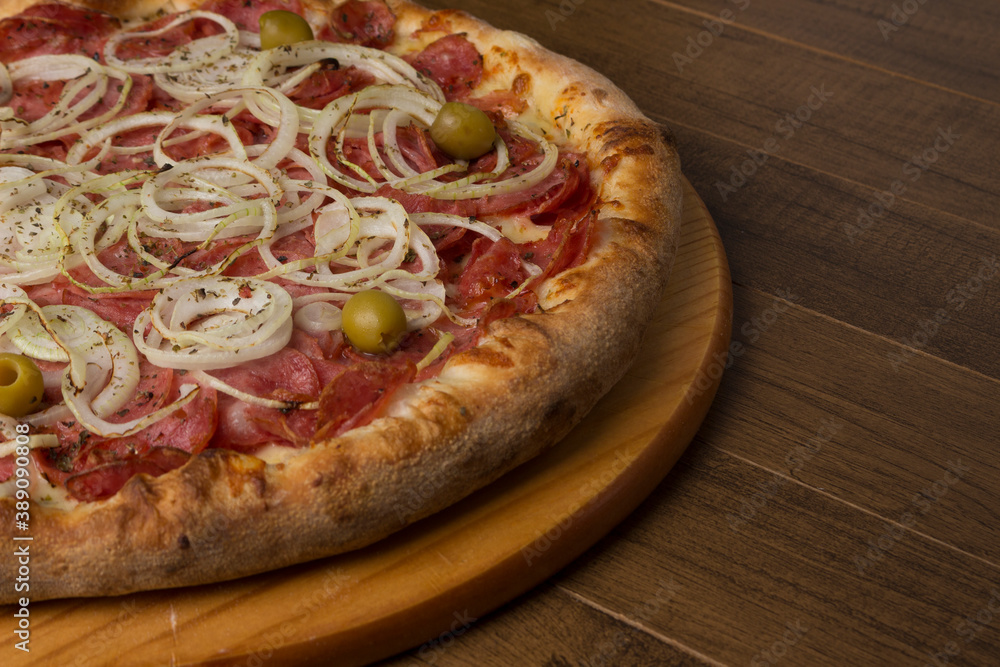 A delicious pepperoni pizza, sliced ​​onions, mozzarella cheese and green olives. Served on a wooden board. Right space for text.