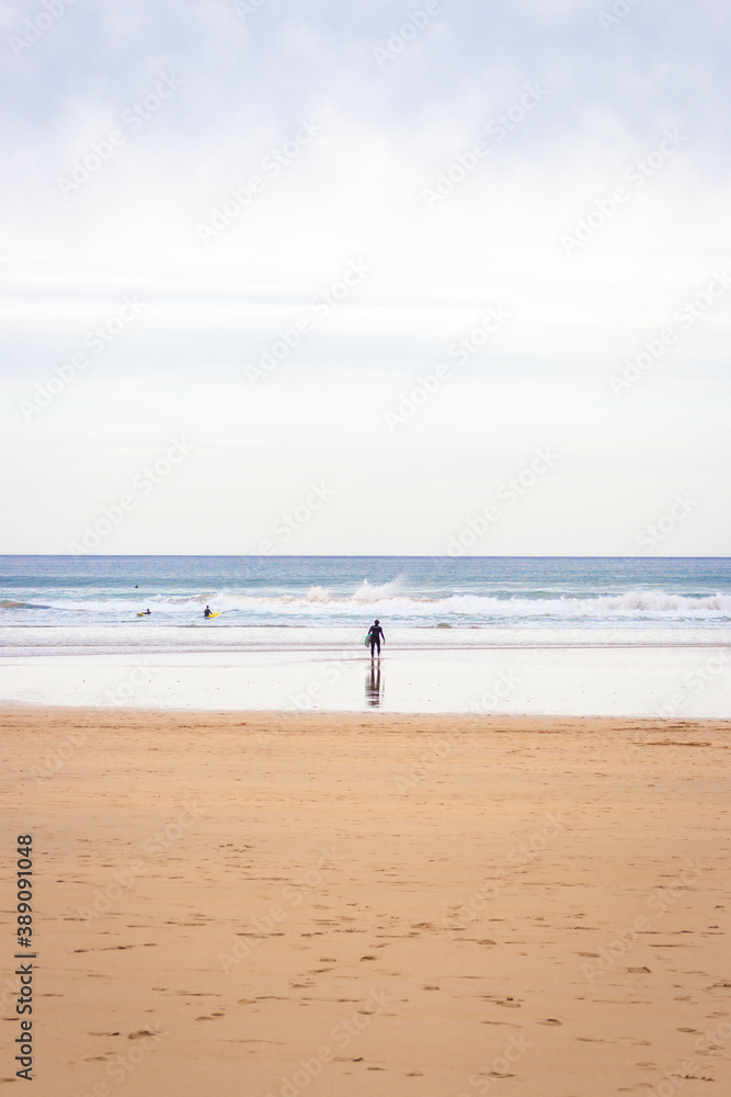 Surfers on wide beach, bay of Biscay. Surf concept. Active people. Idyllic surfing day in Spain. Seascape with waves and surfers. Active lifestyle. Surfers on seaside on cloudy day in autumn.