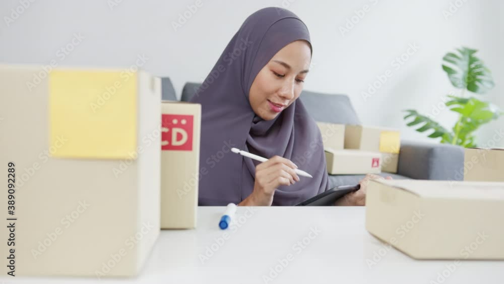 Young Asia muslim businesswoman check product purchase order on stock and save to tablet computer work at home office. Small business owner, online market delivery, lifestyle freelance concept. Young Asia muslim businesswoman check product purchase order on stock and save to tablet computer work at home office. Small business owner, online market delivery, lifestyle freelance concept.