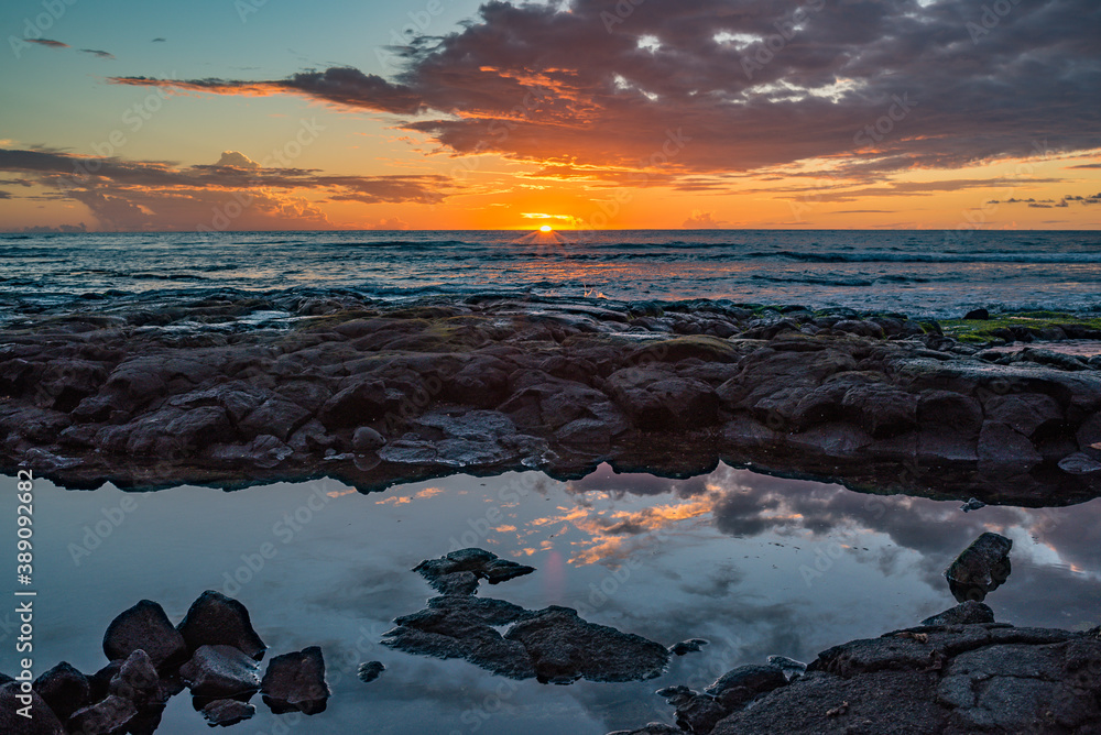 Orange sunset over ocean with waves and lava rock beach shoreline