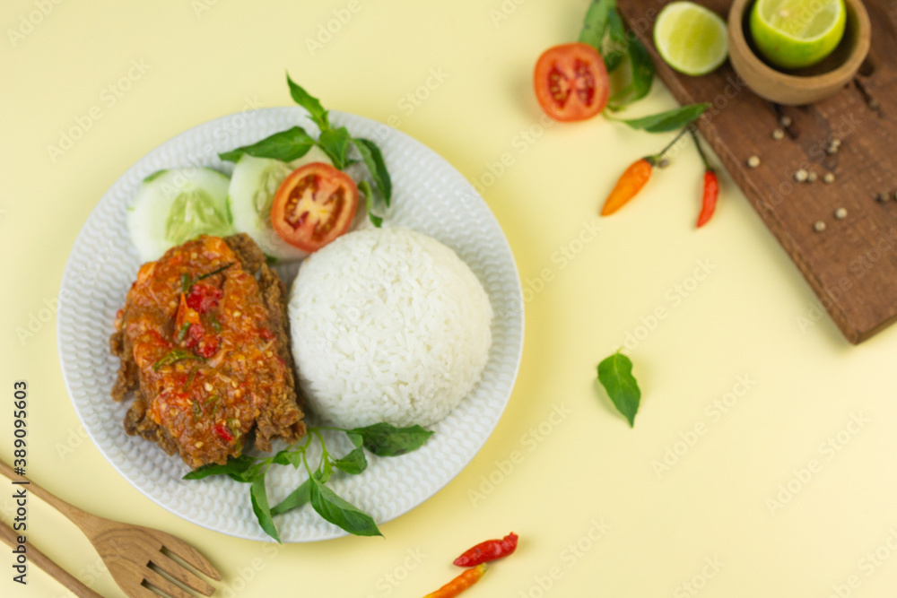 Ayam geprek, Indonesian popular streed food, made from crispy chicken smashed with sambal or chili sauce, eat with rice and cucumber, lettuce, tomato and kemangi. Isolated background, copy space. Ayam geprek, Indonesian popular streed food, made from crispy chicken smashed with sambal or chili sauce, eat with rice and cucumber, lettuce, tomato and kemangi. Isolated background, copy space.