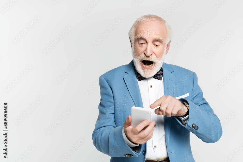Excited senior man pointing with finger at smartphone on blurred foreground isolated on grey Excited senior man pointing with finger at smartphone on blurred foreground isolated on grey