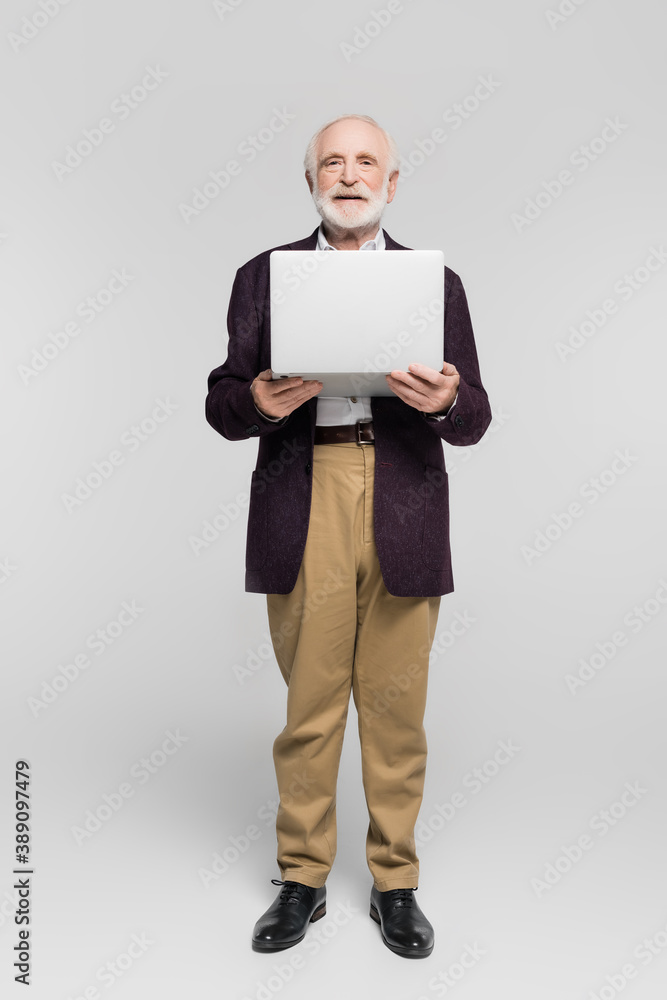 Senior man smiling at camera while holding laptop on grey background Senior man smiling at camera while holding laptop on grey background