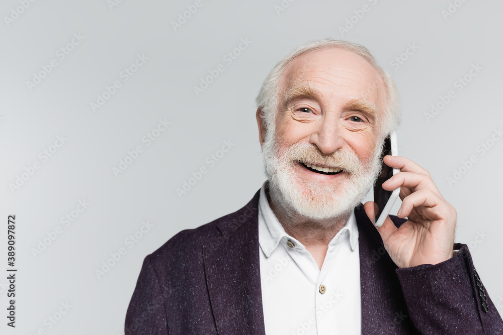 Smiling elderly man talking on smartphone isolated on grey Smiling elderly man talking on smartphone isolated on grey