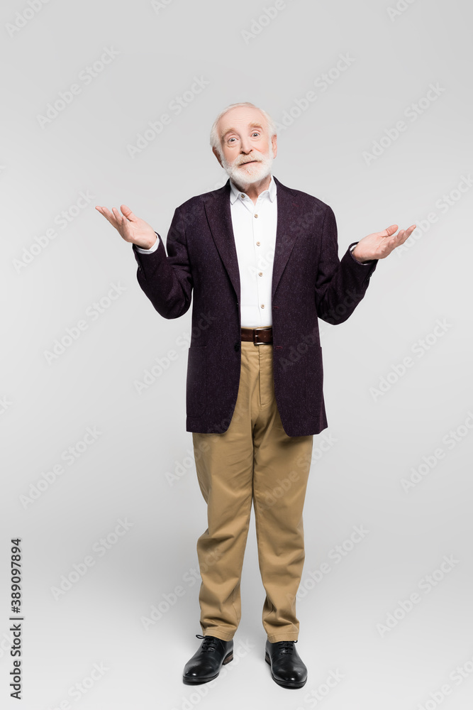 Confused senior man in jacket and shirt showing shrug gesture on grey background Confused senior man in jacket and shirt showing shrug gesture on grey background