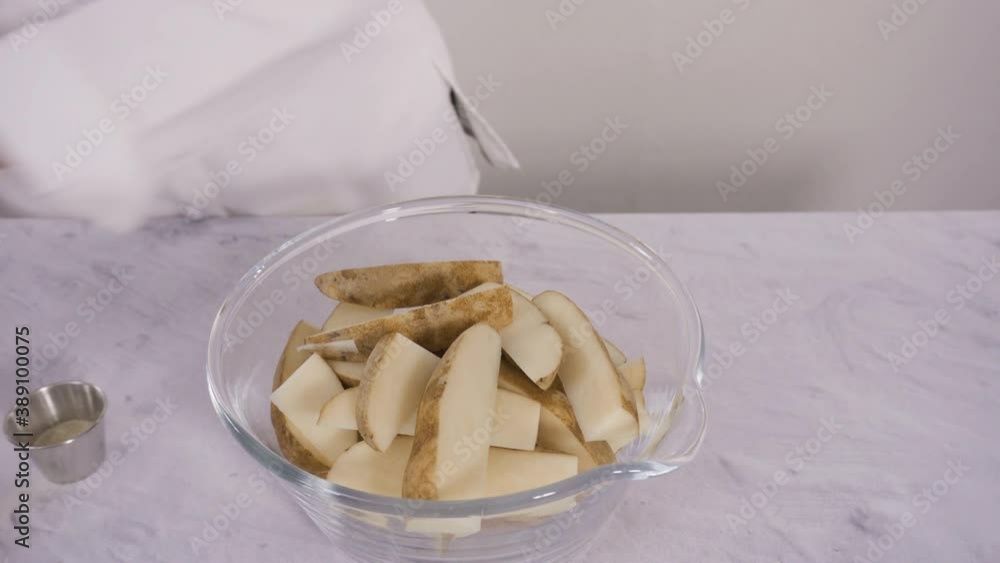 Step by step. Soaking potato wedges in a bowl of water to prepare baked potato wedges with spices.