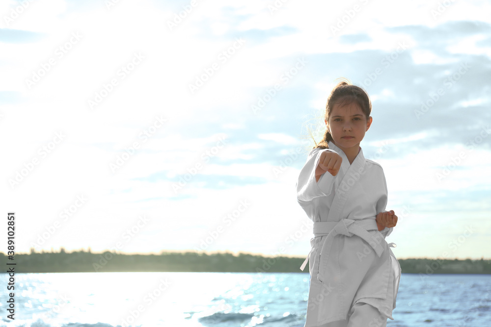 Cute little girl in kimono practicing karate near river Cute little girl in kimono practicing karate near river