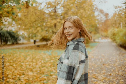 The girl walks in the autumn park. Beautiful blonde looks at the camera and smiles, teen girl on a background of autumn leaves