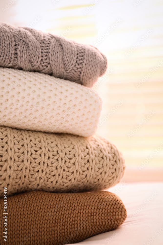 Stack of folded warm sweaters on bed indoors, closeup