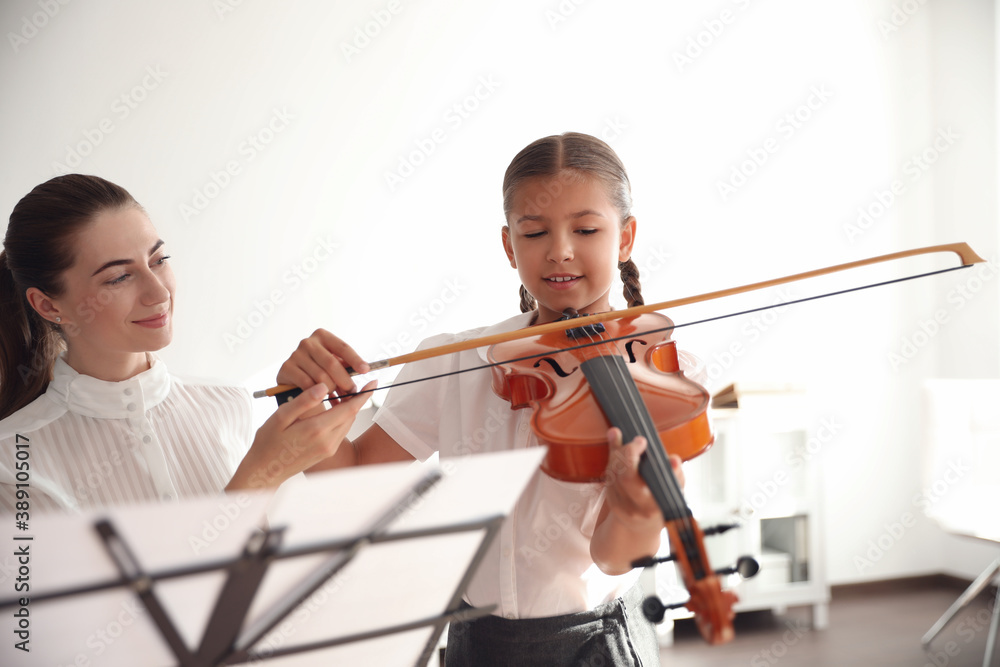 Young woman teaching little girl to play violin indoors Young woman teaching little girl to play violin indoors
